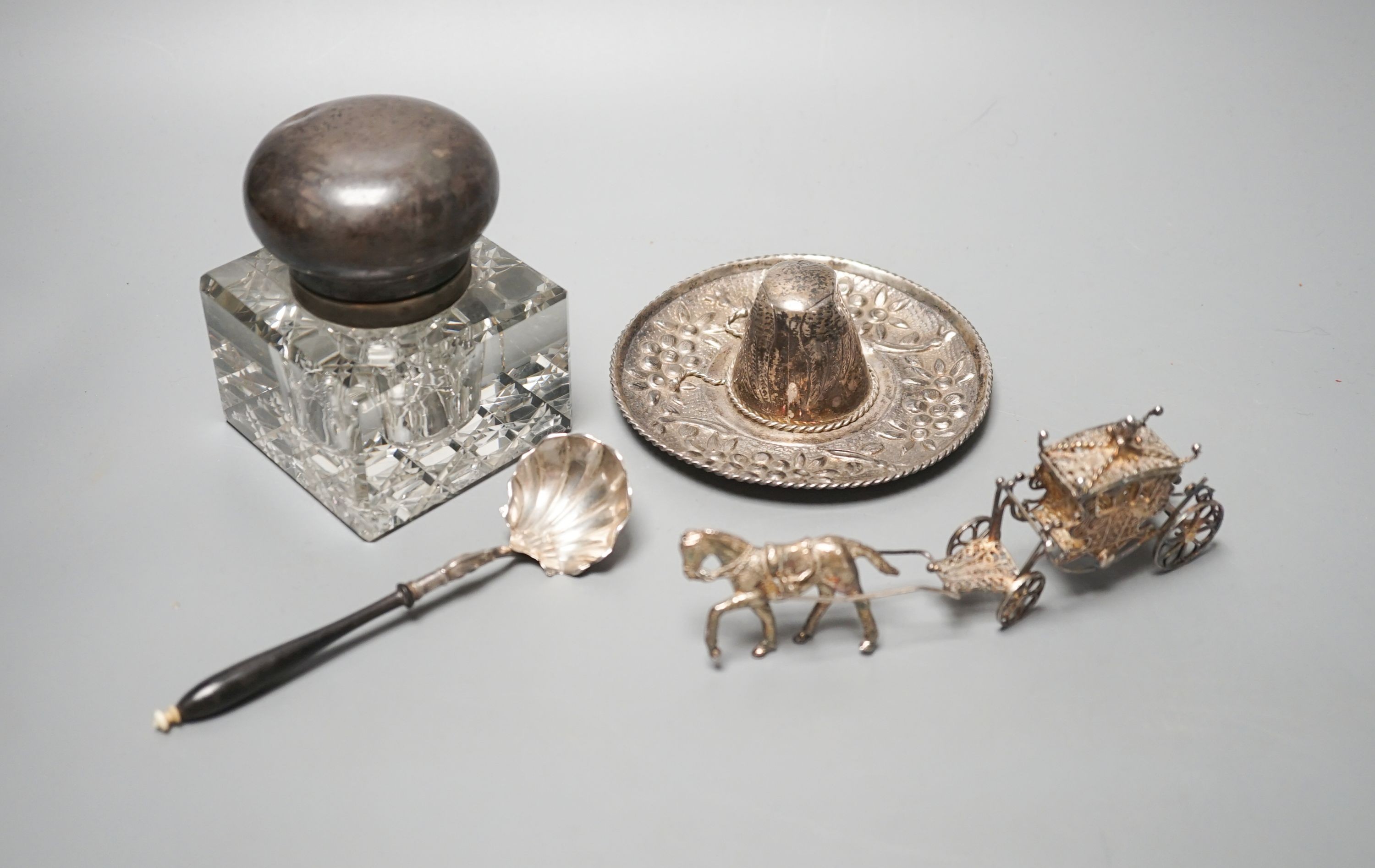 A silver mounted glass inkwell, A Mexican white metal miniature sombrero, a white metal caddy spoon and a filigree horse and carriage.